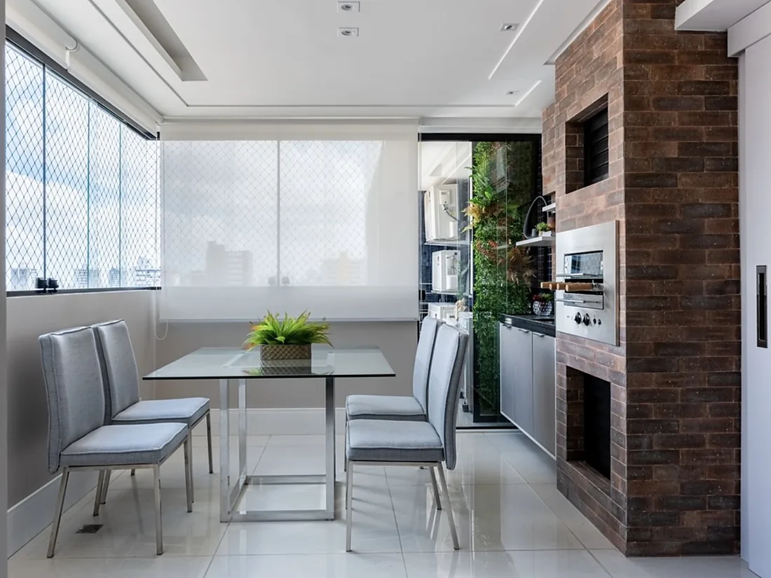 Varanda envidraçada com mesa de jantar e parede de tijolo